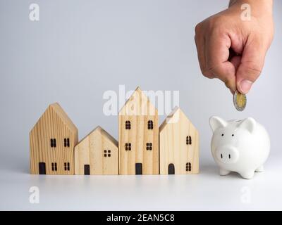 Ein Modell Holzhaus und eine Männerhand mit einer Münze auf weißem Hintergrund. Geschäftskonzept Wohnen. Stockfoto