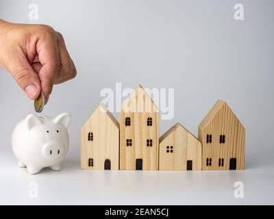 Ein Modell Holzhaus und eine Männerhand mit einer Münze auf weißem Hintergrund. Geschäftskonzept Wohnen. Stockfoto