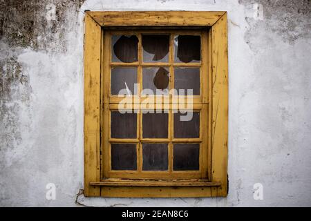 Gelbe Fenster im Retro-Stil mit zerbrochenem Glas an schmutzigen, beschädigten weißen Wänden. Detail Fenster in verlassenen ländlichen Haus Stockfoto