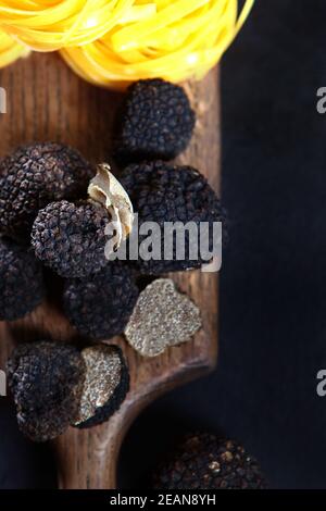Schwarze Trüffel und Nudeln in Form von Nestern auf einem Holzbrett. Schwarze Trüffelsaison. Der teuerste und würzige Pilz. Draufsicht. Stockfoto