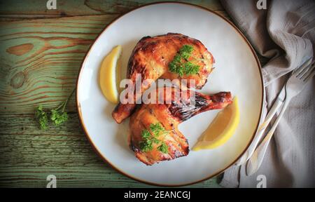 Gegrillte Hähnchenschenkelvierteln mit Zitrone, Petersilie auf weißem Teller auf Holzbrettern. Hintergrund für das Essen. Draufsicht Stockfoto