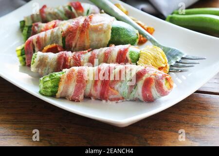 Gegrillte Zucchini-Pommes in einem Speck auf weißem Teller gewickelt Stockfoto