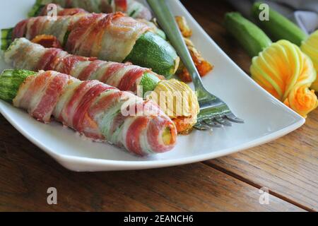 Gegrillte Zucchini-Pommes in einem Speck auf weißem Teller gewickelt Stockfoto