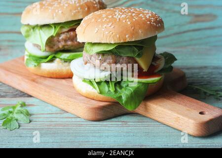 Hausgemachter Hamburger mit Rindfleisch, Zwiebeln, Gurken, Salat, Käse, Spinat und Gewürzen. Frische Burger Nahaufnahme auf Holz Schneidebrett Stockfoto