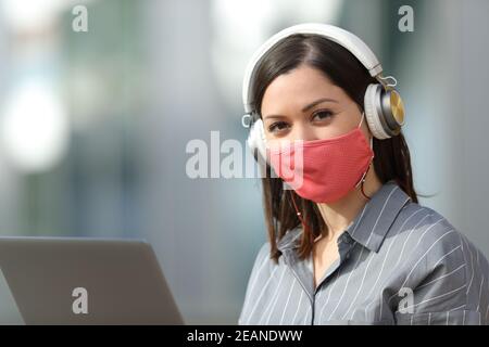 Frau mit Maske Laptop und Kopfhörer schaut Sie an Stockfoto