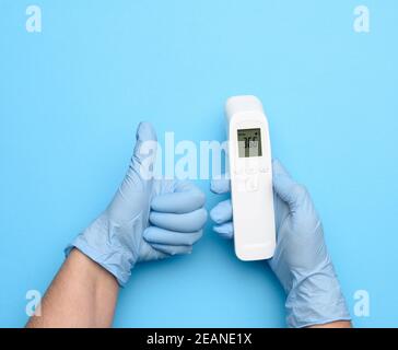 Zwei Hände in blauen Latexhandschuhen halten ein elektronisches Thermometer Zum Messen der Temperatur Stockfoto