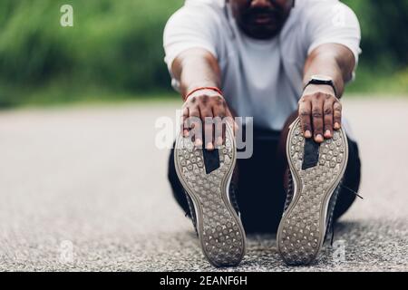 Sport Läufer schwarz Mann tragen Uhr er sitzt ziehen Zehe Füße dehnen Beine und Knie Stockfoto