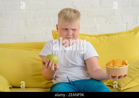 Junge hält Apfel und Chips, und kann nicht entscheiden, was zu essen Stockfoto