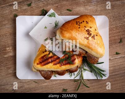 Heiße Brötchen mit Würstchen, eingelegte Gurken und Dill auf einem weißen Teller mit einer Serviette auf einem braunen Tisch. Draufsicht. Stockfoto