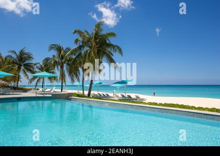 Grand Cayman Beach Liegestühle Blaue Sonnenschirme am Wasser's Edge, Cayman-Inseln, Grand Cayman, Seven Mile Beach - Cayman-Inseln, Hintergründe, Strand Stockfoto