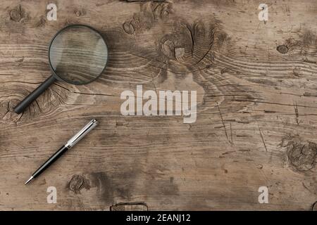 Vergrößerungsglas und ein Stift, der auf einer alten Holzstruktur liegt Stockfoto