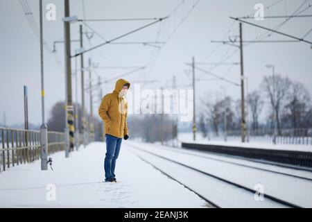 Verschneite Bahnhof während frostigen Tag. Mann, der auf dem Bahnsteig steht und auf einen verspäteten Zug wartet. Stockfoto