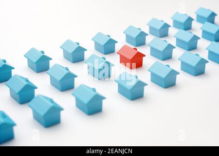 Miniatur rot Modell Haus unterscheidet sich von Gruppe blau Spielzeug gleichen Typ Häuser auf weiß. Auswahl Immobilien oder Immobilienmarkt in Cottage Village oder Stockfoto