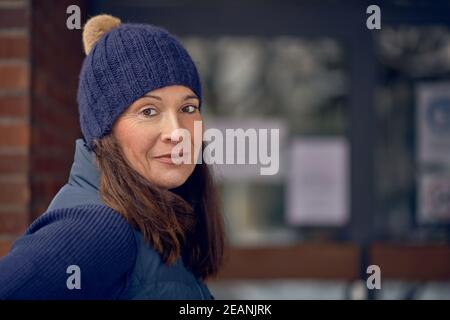 Attraktive freundlich lächelnde Frau im blauen Winter Outfit mit gestrickt beanie Hut und warme Jacke in einem Nahaufnahme Kopf Und Schultern im Freien Porträt Stockfoto