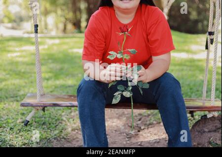 Eine Frau in einem roten Hemd sitzt eine Rose auf Eine Schaukel Stockfoto