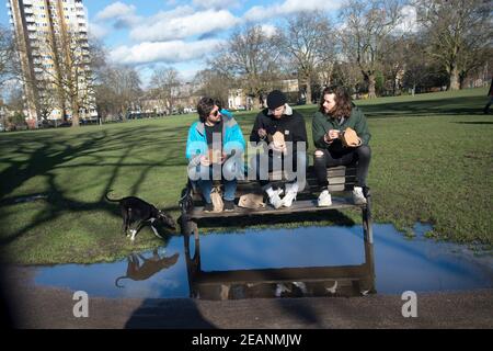 London, Hackney. London Fields. Drei Freunde essen im Park zu Mittag und halten ihre Füße trocken. Stockfoto