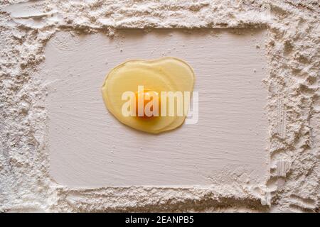 Mehl bestreut auf einem Holztisch, mit einem glatten rechteckigen Druck und ein rohes Ei in der Mitte. Speicherplatz kopieren. Stockfoto