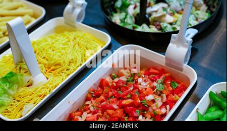 Salatbuffet im Restaurant. Frisches Salatbuffet zum Mittag- oder Abendessen. Gesunde Ernährung. Gehackte Tomaten und gelbe Nudeln in einer weißen Schüssel auf der Theke. Catering-Essen. Bankettservice. Vegetarisches Essen. Stockfoto