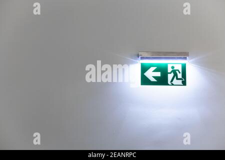 Grün beleuchtetes Notausgangsschild an einer weißen Wand Ein Gebäude Stockfoto