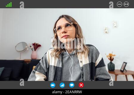 Computerbildschirm Ansicht einer jungen Frau, die Brille und Kopfhörer trägt, mit einem durchdachten Blick, mit einem Videoanruf. Studentin mit Teleconferenc Stockfoto