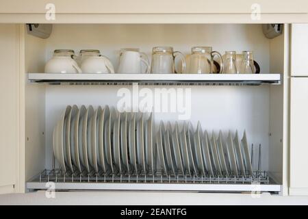 Regal zum Trocknen von Geschirr in der modernen Küche. Sauberes, gewaschenes weißes Glas und Keramikgeschirr auf Metallregal im Küchenschrank. Stockfoto