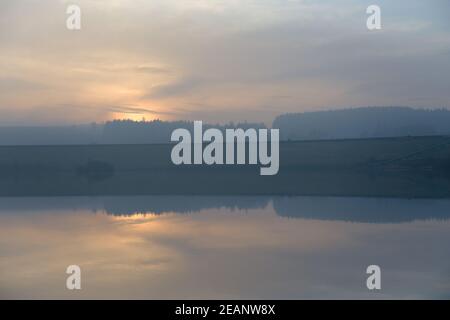 12 Menschen laufen vor einer Staumauer entlang Ein verschwommener Sonnenuntergang in der Dämmerung Stockfoto