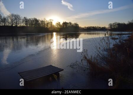 Wintersonnengang über einer Seenoberfläche, die die gefrorenen Eismuster auf dem Wasser hervorhebt. Stockfoto