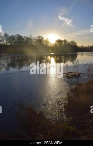 Wintersonnengang über einer Seenoberfläche, die die gefrorenen Eismuster auf dem Wasser hervorhebt. Stockfoto