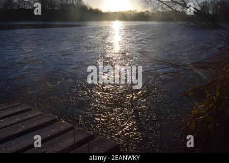 Wintersonnengang über einer Seenoberfläche, die die gefrorenen Eismuster auf dem Wasser hervorhebt. Stockfoto