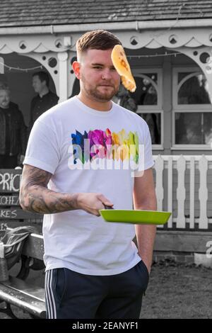 Mann wirft Pfannkuchen auf Pfannkuchen auf dem Pavillon Pfannkuchen Rennen am Shrove Dienstag in Christchurch, Bournemouth, Dorset UK im März Stockfoto