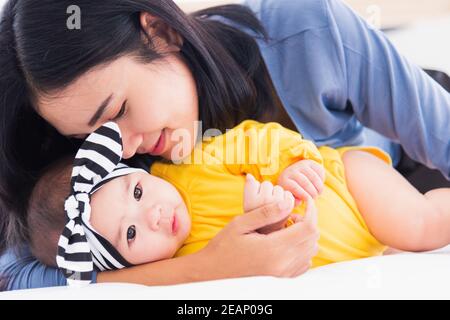 Mutter küsst ihr neugeborenes Baby in einem weißen Bett Stockfoto