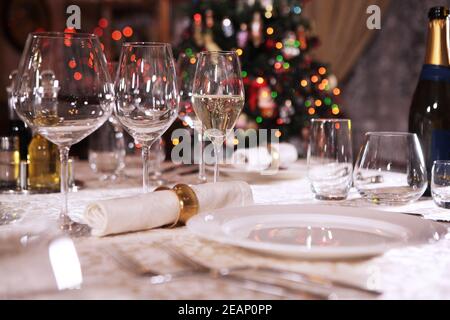 Ein Glas Champagner, halb gefüllt, steht auf einem schön gedeckten Tisch.das Konzept der Feier. Der Weihnachtsbaum ist nicht im Fokus. Flanke. Speicherplatz kopieren. Stockfoto