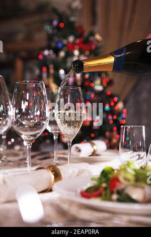 Schön gedeckten Tisch für das neue Jahr. Champagner wird in ein hohes Glas gegossen. Alkoholisches Schaumgetränk. Speicherplatz kopieren. Stockfoto