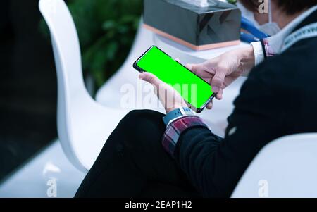 Asiatische Person Hand hält Smartphone mit leeren Touchscreen-Display. Menschen sitzen und verwenden Mobiltelefon für die Kommunikation in Unternehmen und Unternehmen. Die Leute tragen Anzüge und Smartwatch, die ihre E-Mails abrufen. Stockfoto