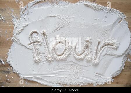 Das handschriftliche Wort Mehl ist auf gefrästem, gesiebenem Weizen geschrieben, der auf einem Holztisch bestreut wird. Stockfoto