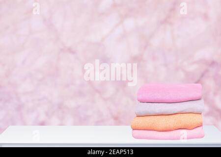 Ein Stapel von bunten, warmen Pullovern auf einem hellen Tisch vor abstraktem, unscharfem rosa Hintergrund. Herbst- und Frühlingskleidung. Platz für die Montage der Produktanzeige. Stockfoto