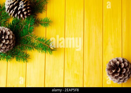 Rahmen mit Tannenzweigen und Zapfen auf altem gelbem Holzbrett. Leerzeichen für Text. Draufsicht. Stockfoto