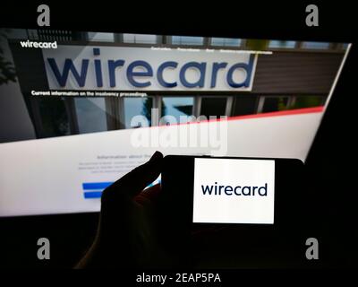 Person mit Mobiltelefon mit Logo des deutschen Zahlungs- und Finanzdienstleisters Wirecard AG vor der Webseite. Fokus auf Handy-Display. Stockfoto