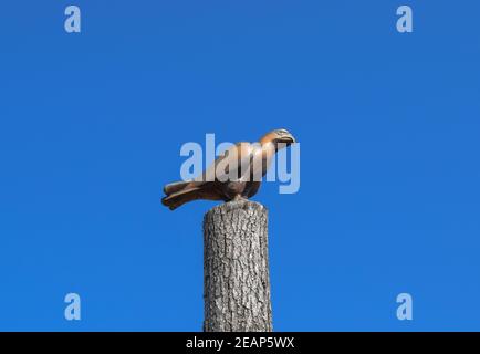 Figur eines Falken auf einem Baumstumpf gegen den blauen Himmel. Figuren von Tieren aus Holz. Holzschnitzerei Stockfoto