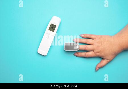 Prozess der Messung des Sauerstoffgehalts im Blut an einem Finger, neben einem elektronischen berührungslosen Thermometer Stockfoto