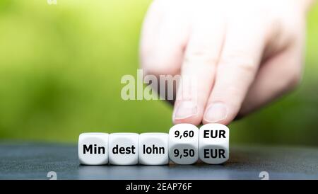 Hand dreht Würfel und ändert den deutschen Ausdruck 'Mindestlohn (Mindestlohn) 9,50 EUR' in 'Mindestlohn (Mindestlohn) 9,60 EUR'. Stockfoto