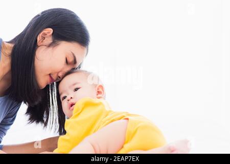 Mutter küsst ihr neugeborenes Baby in einem weißen Bett Stockfoto