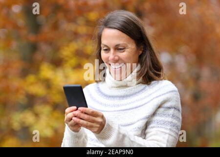 Glückliche Frau mittleren Alters mit Telefon im Herbst in einem parken Stockfoto