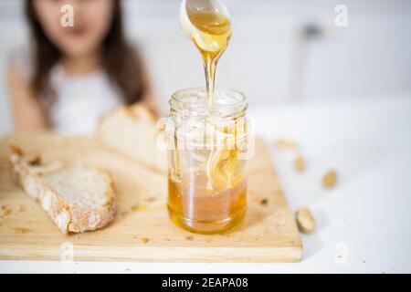 Männliche Hand pflücken Honig aus einem Glas neben einem Brotscheibe Stockfoto