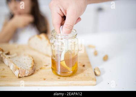 Männliche Hand pflücken Honig aus einem Glas neben einem Brotscheibe Stockfoto