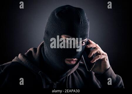 Criminal trägt schwarze Balaclava und Hoodie mit einem Smartphone in Die Dunkelheit Stockfoto