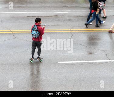 Ein junger Mann schaut auf sein Handy, während er während der jährlichen Open Streets-Veranstaltung in Oklahoma City auf einem Skateboard auf einer Stadtstraße reitet. Stockfoto