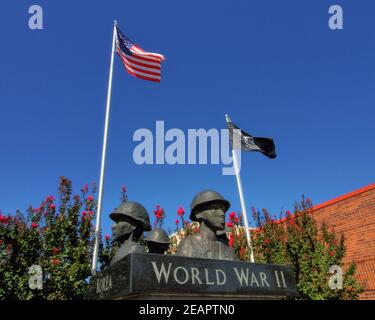 Diese Ansicht zeigt den oberen Teil der Veteranen-Gedenkstatue neben dem Rathaus in der Innenstadt von Tecumseh Oklahoma, mit einer schwarzen MIA und einer amerikanischen Flagge. Stockfoto