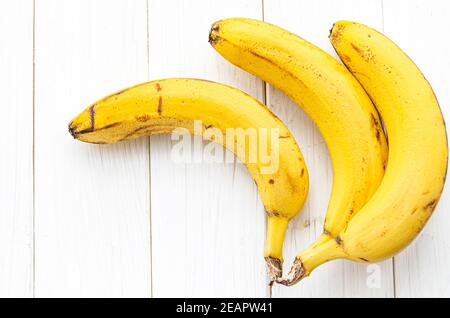Reife gelbe Bananen liegen auf einem weißen Holztisch Stockfoto