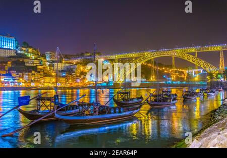 Nachtansicht von Holzbooten in Porto mit Luis I Brücke im Hintergrund, portugal. Stockfoto